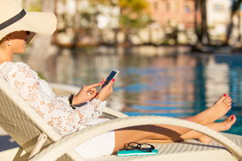 Woman using smartphone to connect to hotel WiFi at the pool